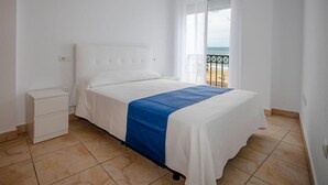 Une chambre à coucher comprenant un lit, une table de chevet, une fenêtre donnant sur la plage et un balcon avec une balustrade.