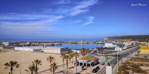 A coastal marina with boats docked, a sandy beach, and a road leading to a building with a green roof. - Hostal Luz del Sol Barbate (Barbate)