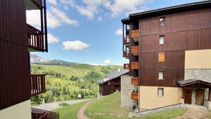 Un edificio de varios pisos con balcones, fachada de piedra y vistas a un paisaje montañoso.