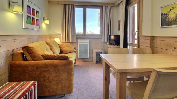 Una habitación acogedora con sofá, mesa de comedor, televisor y ventana con cortinas.