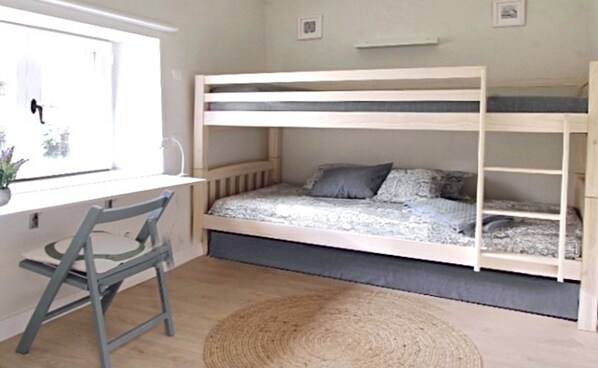 A bunk bed room with a desk and chair, a window, and a woven rug.