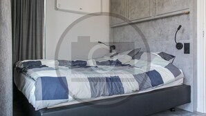 Ein modernes Schlafzimmer mit Bett, Nachttisch, Lampe und einer an der Wand montierten Bedieneinheit.