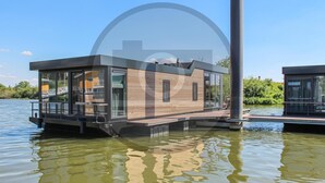 Ein modernes schwimmendes Haus mit großen Fenstern, einem Deck und einem Wasserabschnitt im Hintergrund.