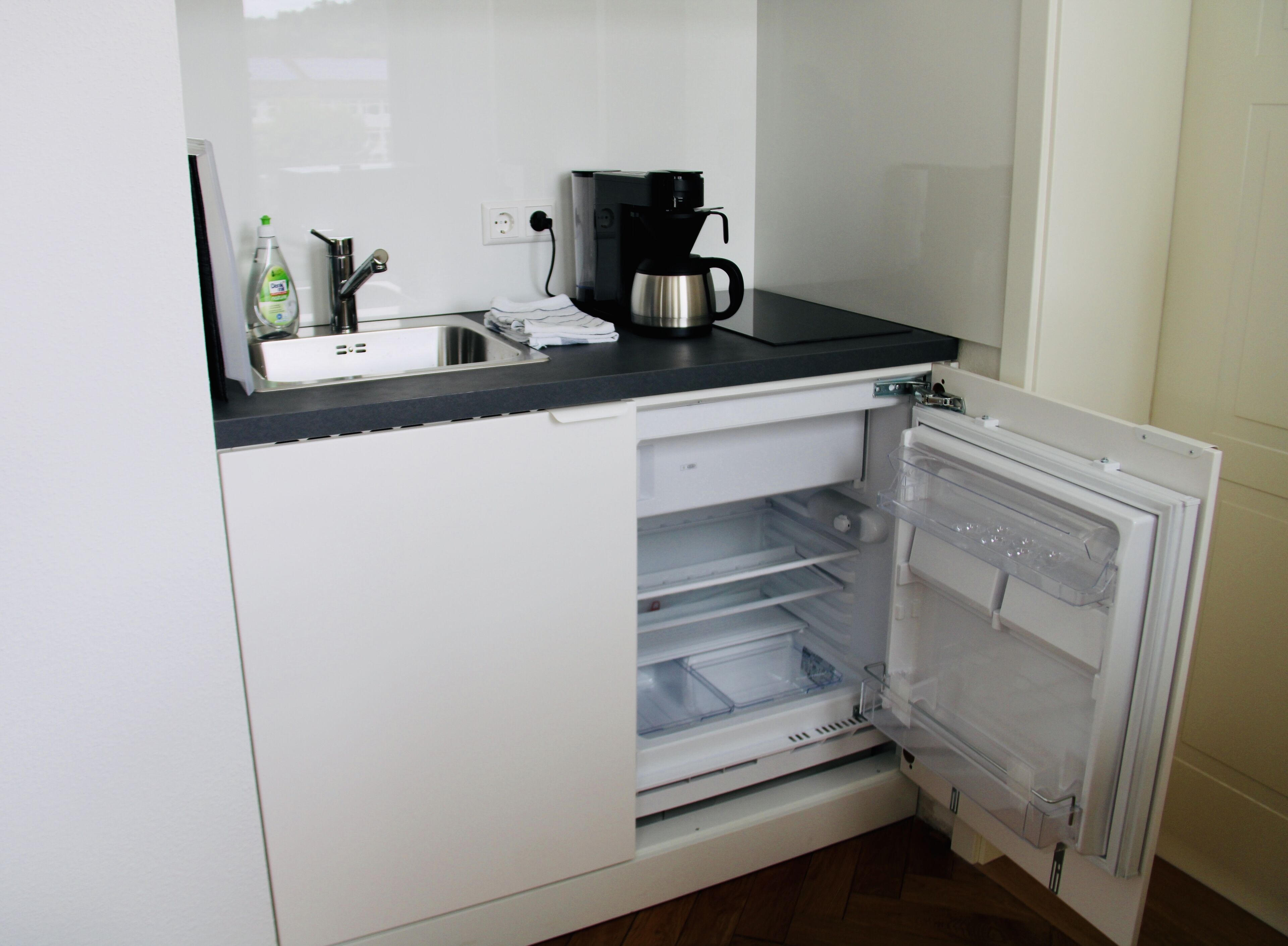 A compact kitchen with a built-in refrigerator, a coffee maker, and a sink.