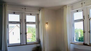 Une pièce avec un radiateur blanc, un petit tabouret blanc, une chaise bleue et une fenêtre donnant sur un paysage verdoyant.