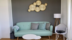 Un salon moderne avec un canapé de couleur turquoise, une table basse ronde blanche, un tapis à motifs et un élément décoratif mural.