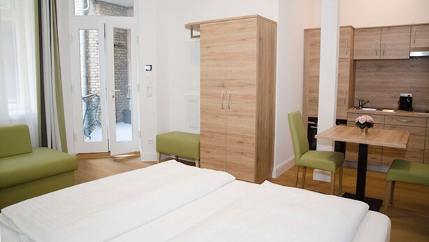 Ein modernes Hotelzimmer mit einem großen Bett, einem grünen Sofa, einem Holzschrank, einem Esstisch mit Stühlen und einer Küchenzeile.