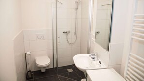 Ein Badezimmer mit Toilette, einer Dusche mit Glastür und einem Waschbecken mit Spiegel.