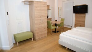 Ein Hotelzimmer mit einem Bett, einem Schreibtisch mit zwei Stühlen, einem Kleiderschrank und einem Fernseher an der Wand.
