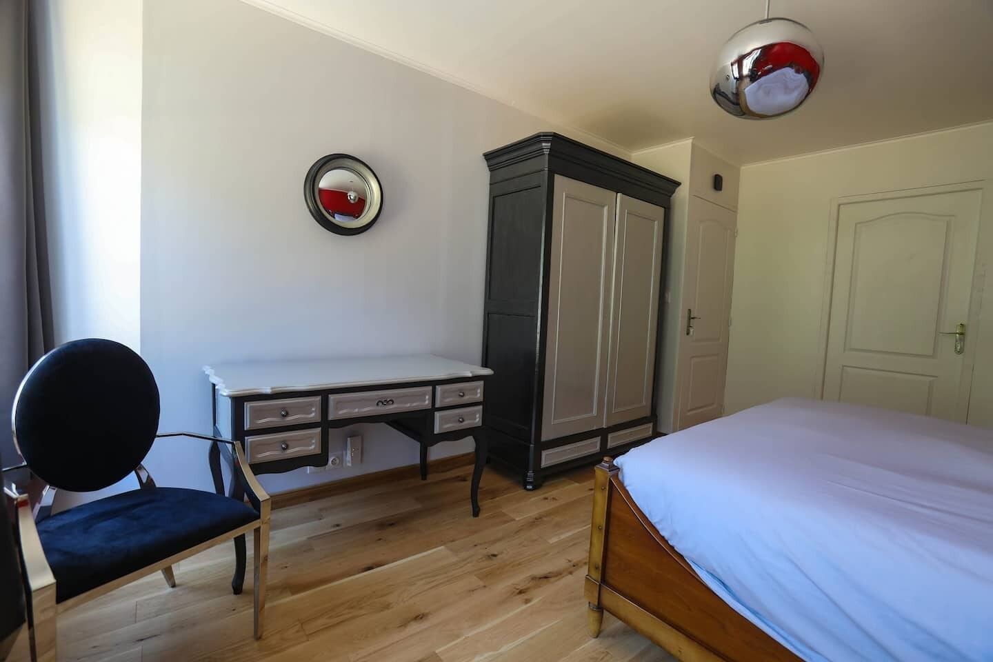A bedroom with a bed, a desk, a chair, a wardrobe, and a mirror.