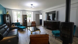 Un salón amplio con un sofá negro, sillones turquesa, una mesa de centro de vidrio y una estufa de leña.