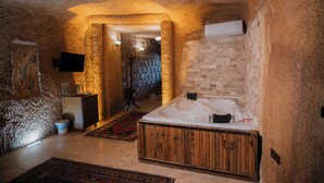 A spa room with a wooden bathtub, a massage table, and a stone wall. - Cappadocia Cave Lodge (Nevsehir)