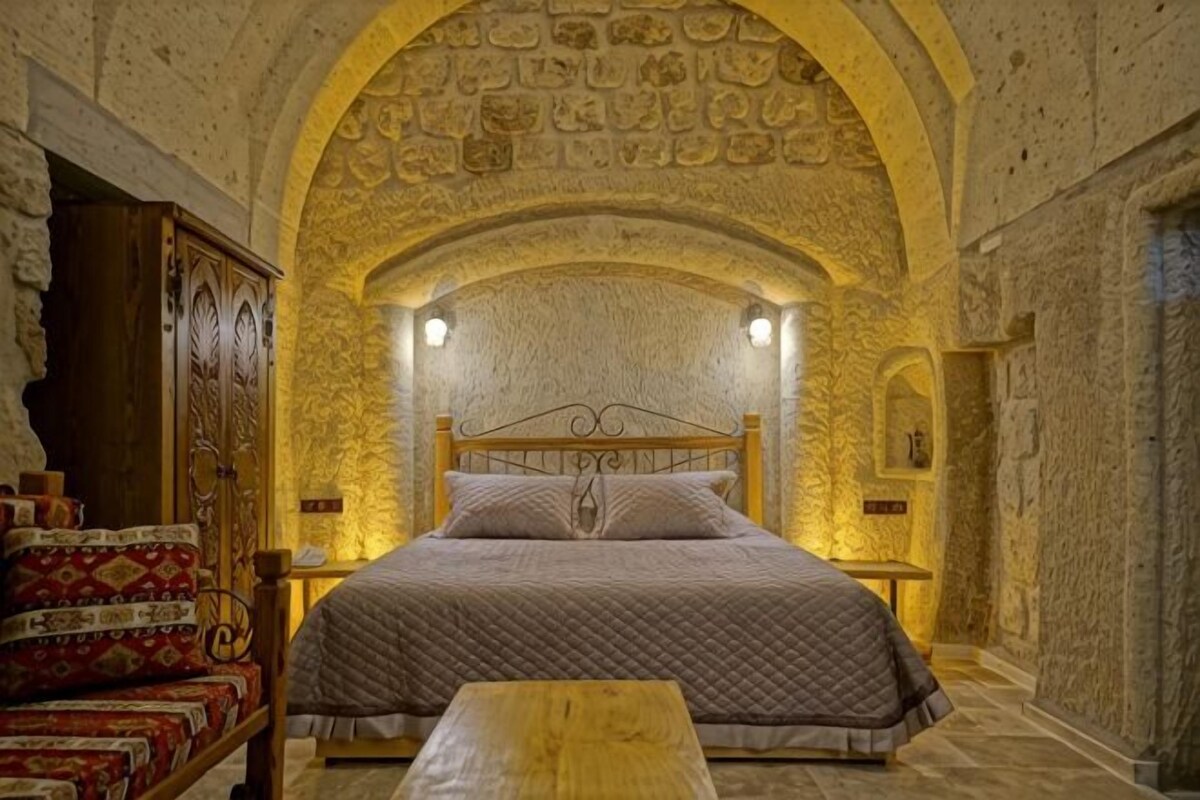 Un dormitorio con pared de piedra, una cama de madera, una mesita de noche y un banco.