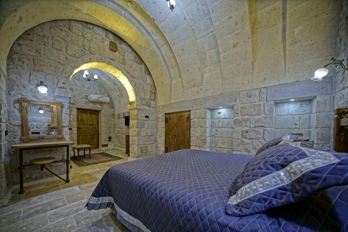 Una habitación de paredes de piedra con una cama, un banco de madera y un escritorio.