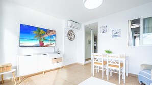 A modern living room with a flat-screen TV, a dining area with a table and chairs, a white cabinet, and a ceiling fan.