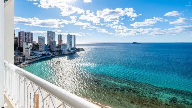 A coastal cityscape with high-rise buildings, a clear blue sky, and a calm sea.