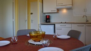 A dining area with a round table set for four, a coffee maker on the counter, and white cabinets above the sink. - Charming 2-Room Apartment Near Sea in Argelès-sur-Mer (Argelès-sur-Mer)