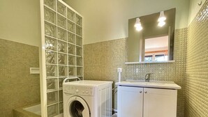 A laundry room with a front-loading washing machine, a sink, and a mirror above it. - Charming 2-Room Apartment Near Sea in Argelès-sur-Mer (Argelès-sur-Mer)