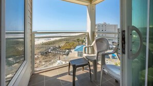 A balcony with a view of the beach, a chair, and a table.