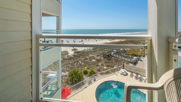 A balcony with a view of the beach and a swimming pool.