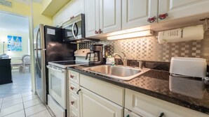 A kitchen with white cabinets, a stainless steel sink, a coffee maker, and a microwave.