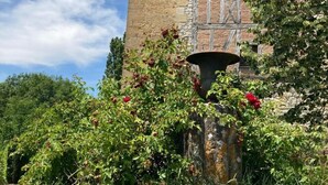En rustik stenbyggnad med en träbalkong, omgiven av frodig grönska och blommande växter.