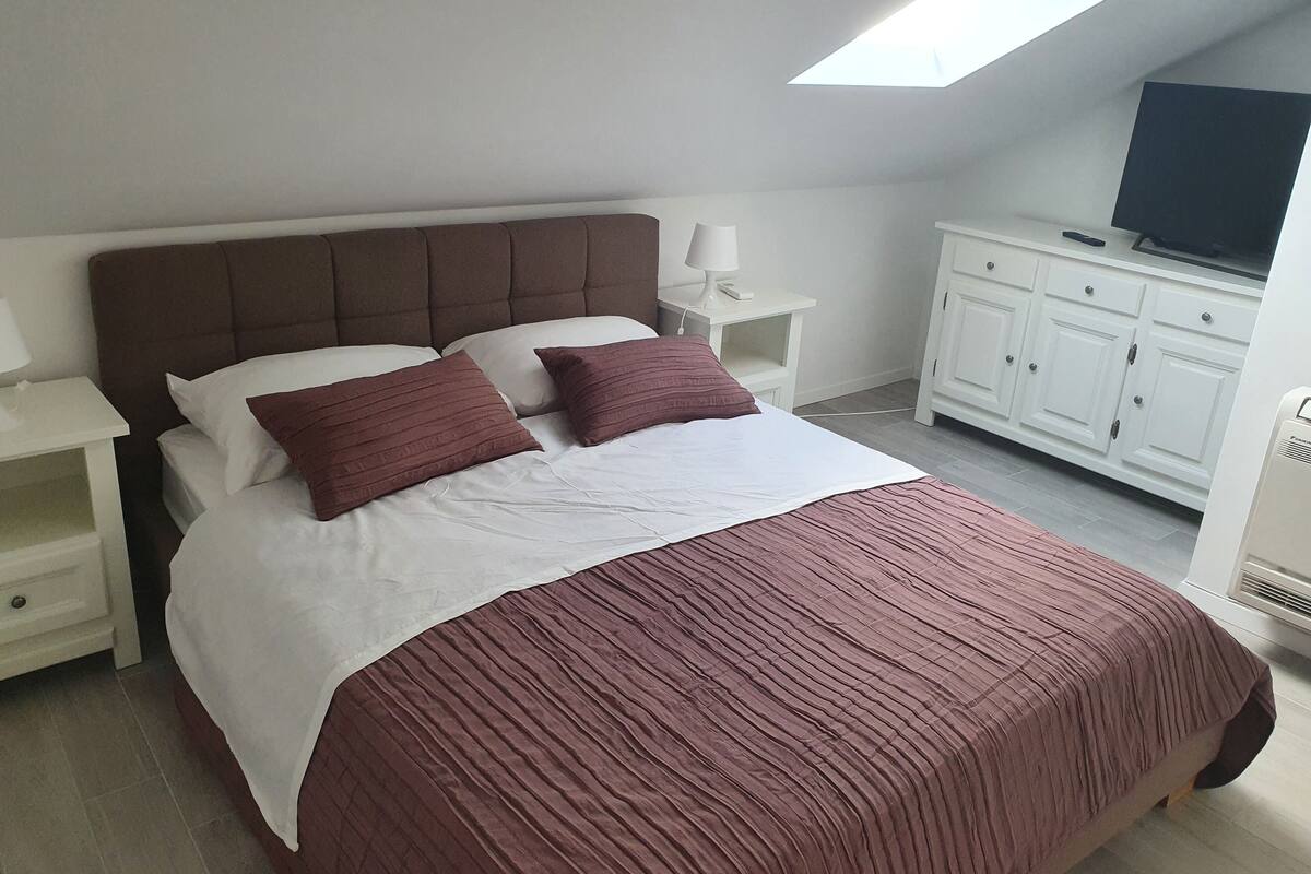 A bedroom with a bed, a nightstand, a lamp, a TV, and a white wardrobe.
