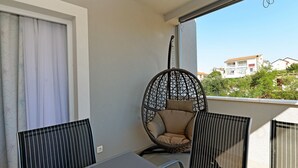 A balcony with a wicker chair, a table, and a view of buildings in the background. - Q apartments (Murter-Kornati)
