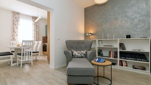 A modern living room with a grey armchair, a small round table with a book, and a bookshelf filled with books. - Q apartments (Murter-Kornati)