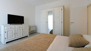 A bedroom with a bed, a TV on a dresser, a wardrobe, and a door leading to another room. - Q apartments (Murter-Kornati)