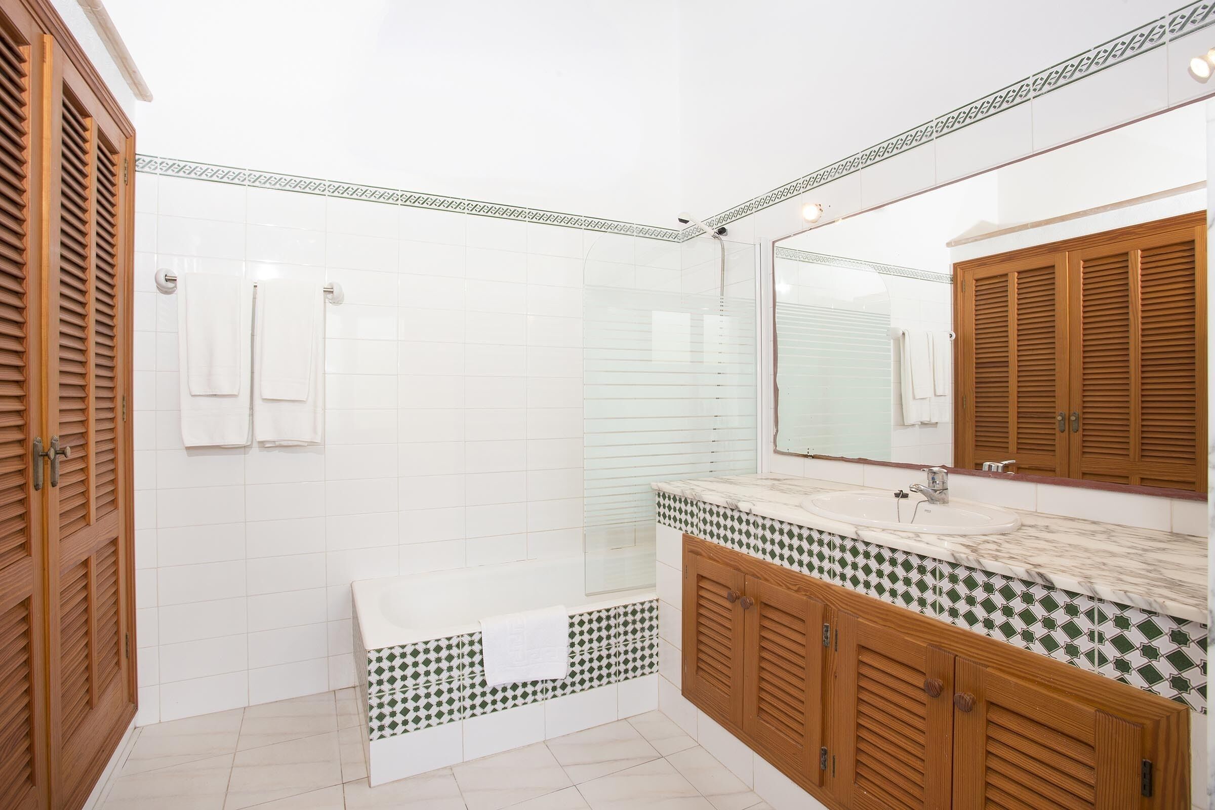 A bathroom with a wooden vanity, a large mirror, and a tiled shower area.