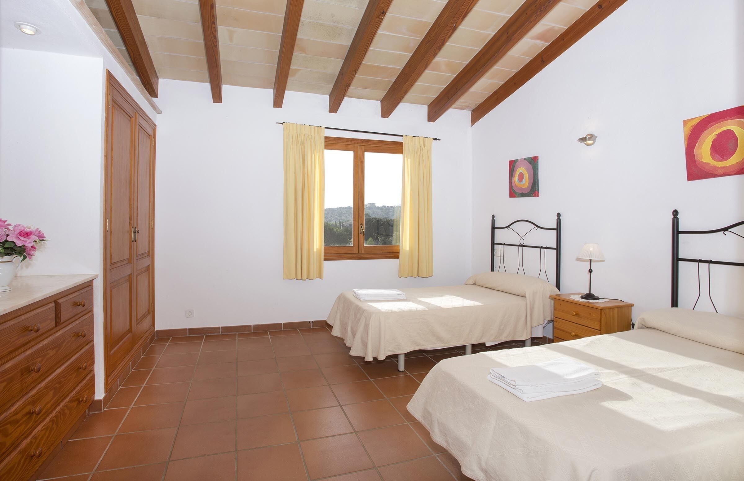 Ein Schlafzimmer mit zwei Einzelbetten, einem Holzschrank, einem Fenster mit Vorhängen und einem Bild an der Wand.