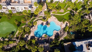 An aerial view of a resort with a unique wavy pool design, surrounded by palm trees and a golf course. - Beachfront cottage - Amazing Walk-up Access to Beach and Patio - E1 North Coast Village (Oceanside)
