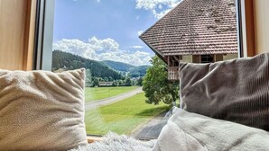 A room with a large window offering a view of a house with a tiled roof and a green landscape.