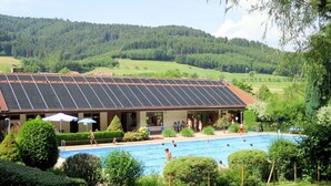 A hotel with a swimming pool, surrounded by lush greenery and hills in the background.