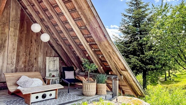 A cozy, wooden-roofed structure with a built-in seating area, including a bench and a chair, and a small table with a lamp.