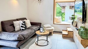 A modern living room with a grey sofa, a round coffee table, and a large window offering a view of greenery.