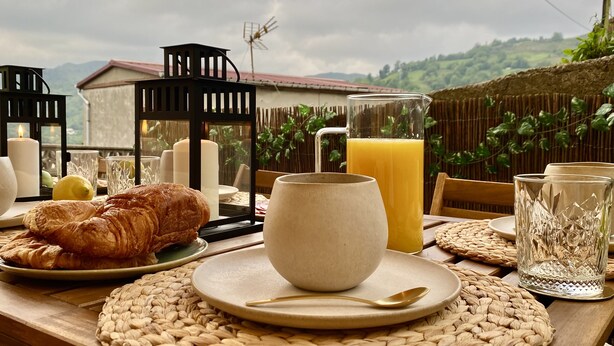 Una mesa de desayuno con croissants, un jarro de jugo de naranja y una vela.
