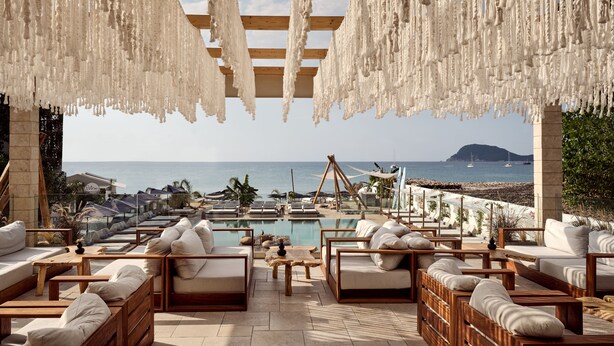 A poolside lounge area with wooden furniture and a view of the sea. - Gardelli Resort (Zakynthos)