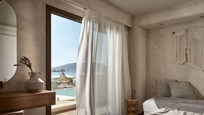 A bedroom with a large window, a wooden bedside table, a bed with a textured blanket, and a wall-mounted macrame piece. - Gardelli Resort (Zakynthos)