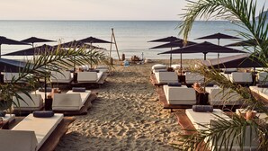 A beachside lounge area with sunbeds and umbrellas, a sandy path leading to the water, and palm trees. - Gardelli Resort (Zakynthos)