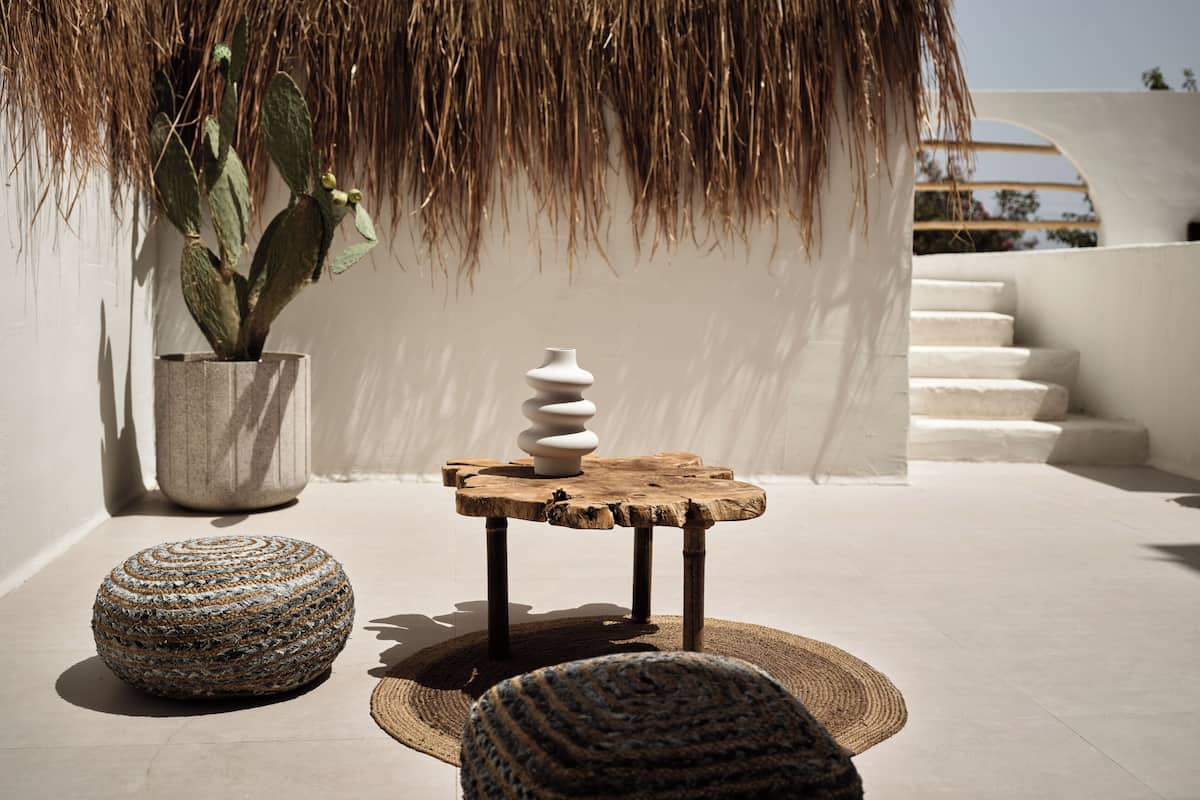 A rooftop terrace with a cactus plant, a white vase, and a wooden table.