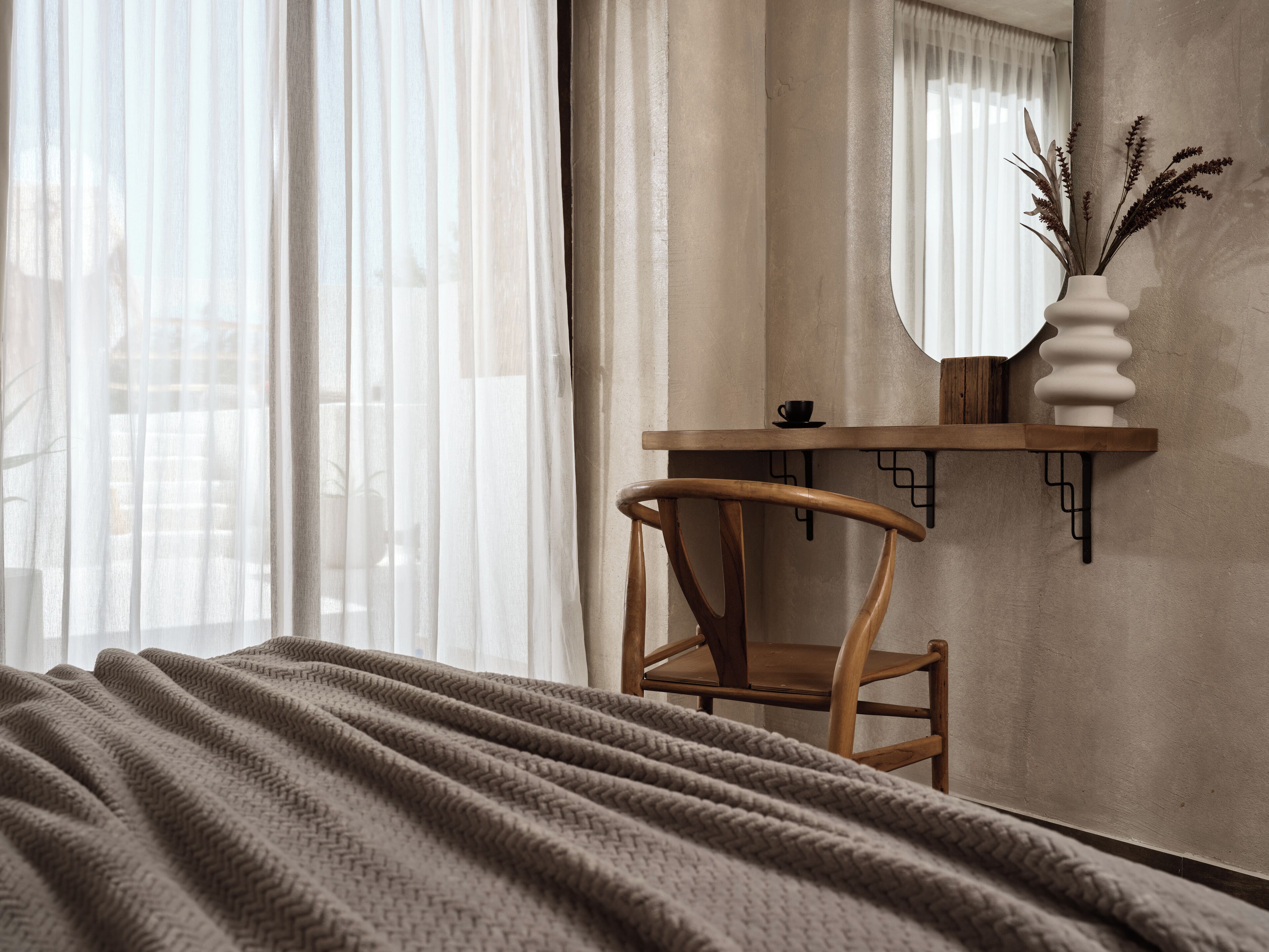 Een slaapkamer met een bed, een stoel, een bureau, een spiegel en een vaas met planten.