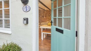 A teal door with a window, a stone wall, a white doorbell, and a number plate. - Host & Stay | Dolphin Cottage 1736 (Whitby)