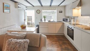 A compact kitchen with white cabinets, a microwave, and a sink. There's a dining area with a table and chairs, and a sofa with a throw pillow. - Host & Stay | Dolphin Cottage 1736 (Whitby)