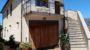 Una casa de dos pisos con un garaje de madera, un balcón con macetas y una escalera que conduce al piso superior.