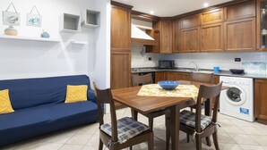 Una cocina compacta con armarios de madera, una mesa de comedor con sillas a cuadros y un sofá azul con cojines amarillos.