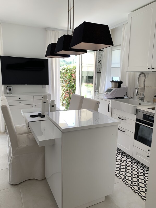 A modern kitchen with a central island, white cabinetry, a flat-screen TV, and a large window with a view of greenery.