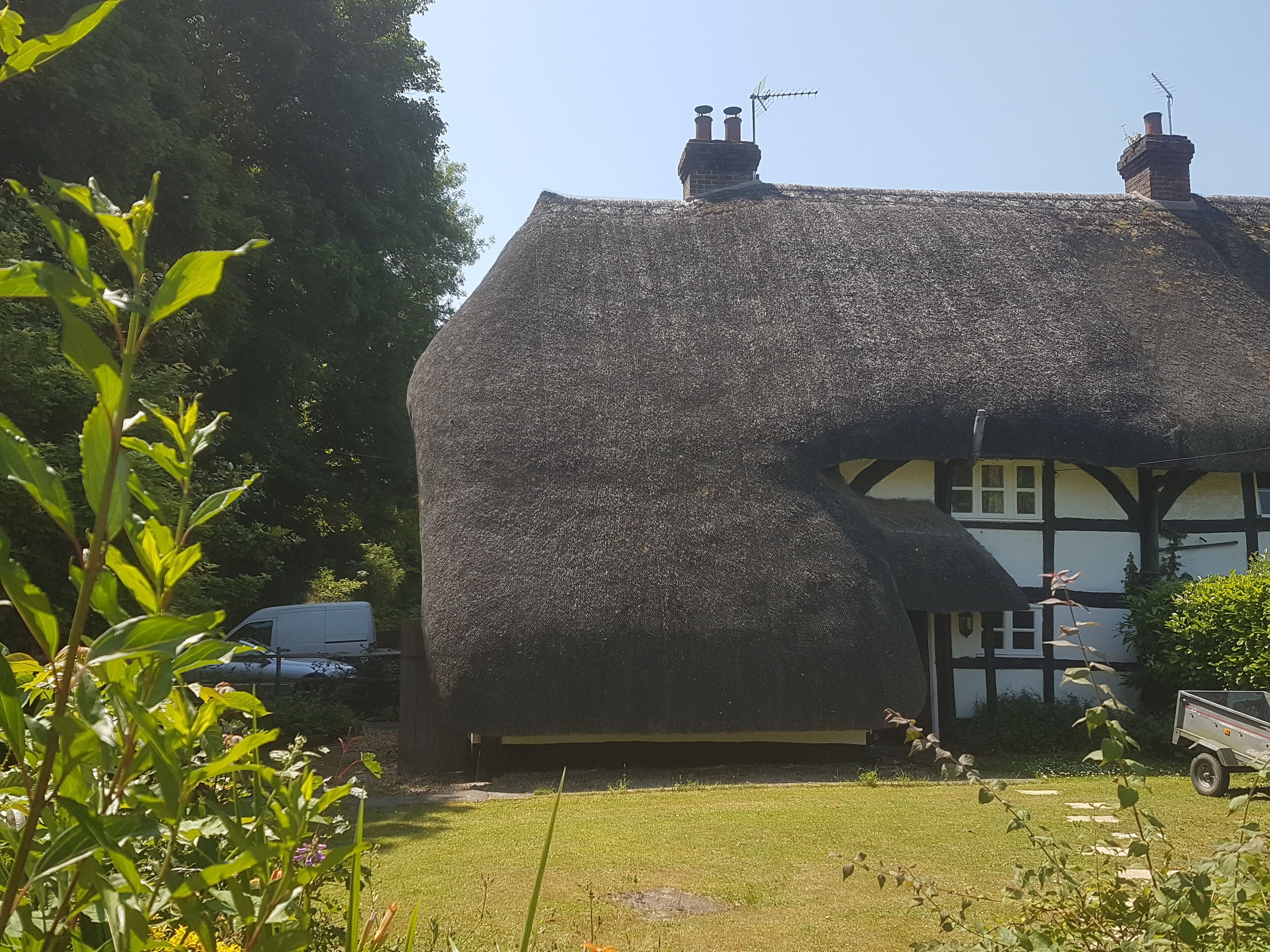 Een rieten dak huis met een zwart-wit vakwerkstructuur, een schoorsteen en een kleine tuin.