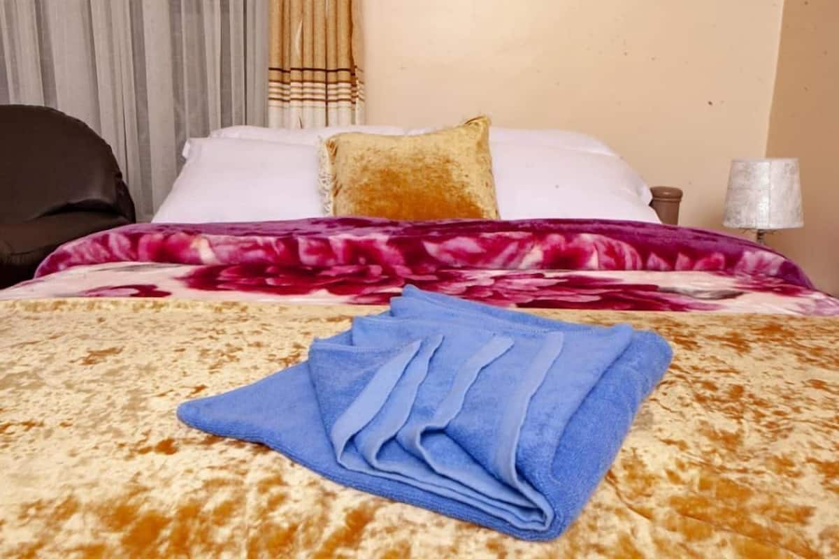 A bed with a patterned bedspread, a blue towel, and a pillow.